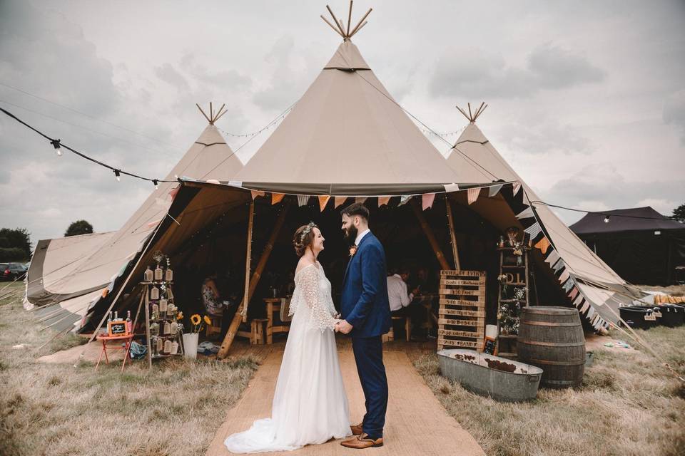 Bride and groom hold hands outside a tipi