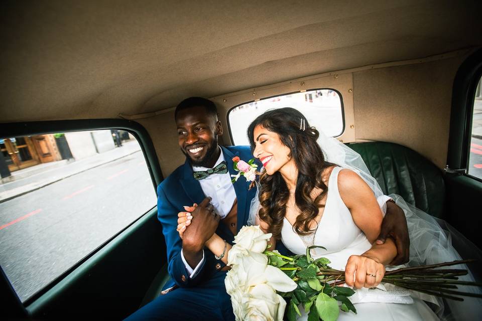 A bride and groom grinning and holding hands in the back of a wedding car