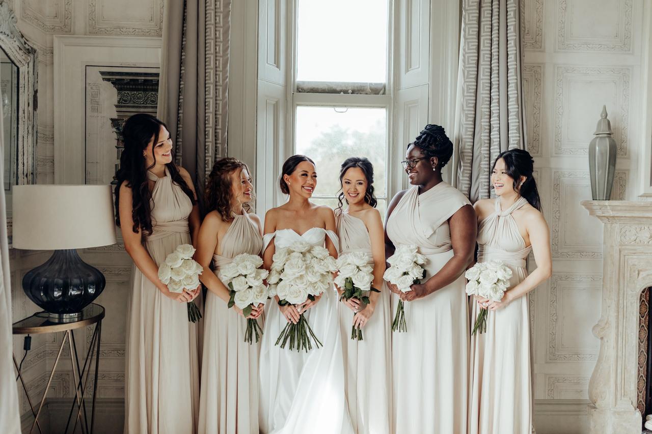 A bride and her bridesmaids, who are dressed in light gold/cream and holding white bouquets.