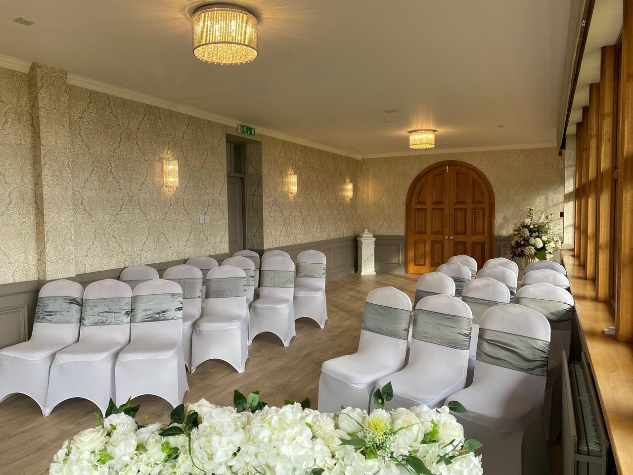 The interior of the ceremony room at The Inn at Charlestown set up for a wedding. It has oak panelled doors and windows with soft lighting and chair covers.