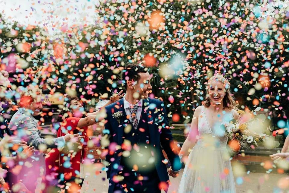 Bride and groom holding hands surrounded by colourful wedding confetti