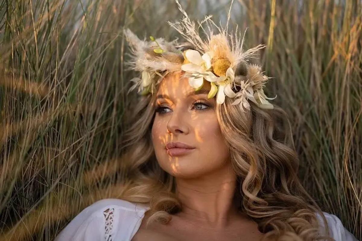 a blonde bride with waxy hair lying in a field of grass whilst wearing a floral pampass grass headband