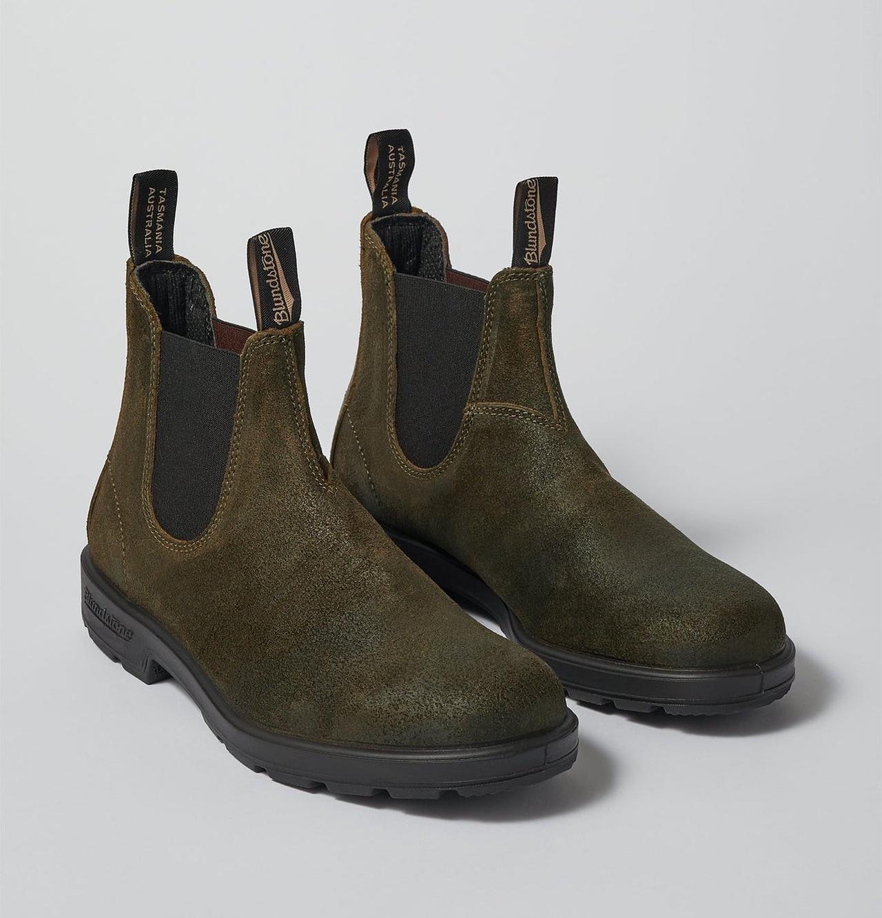 A pair of olive-coloured, waxed suede Chelsea boots on a plain background. 