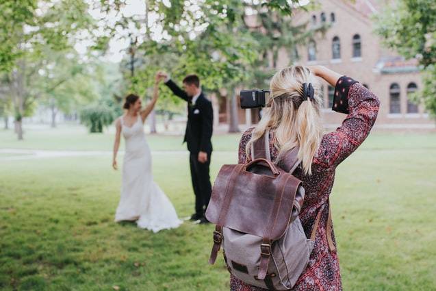 female wedding photographer taking a photo of a bride and groom outdoors