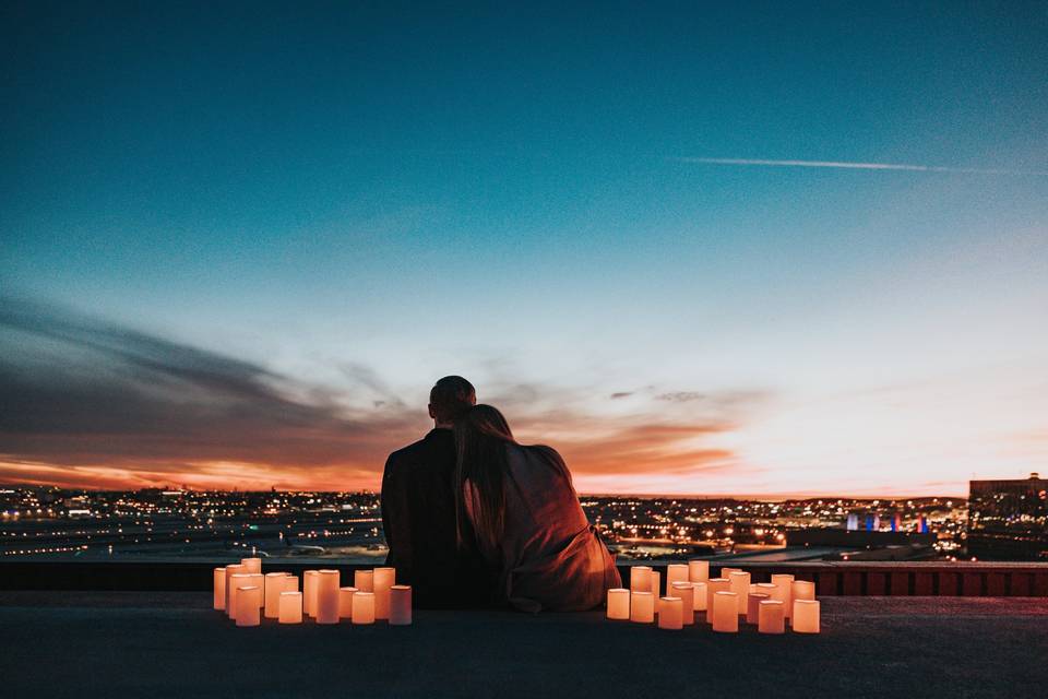 Couple sat together on a rooftop at dusk with candles lit next to them overlooking city lights