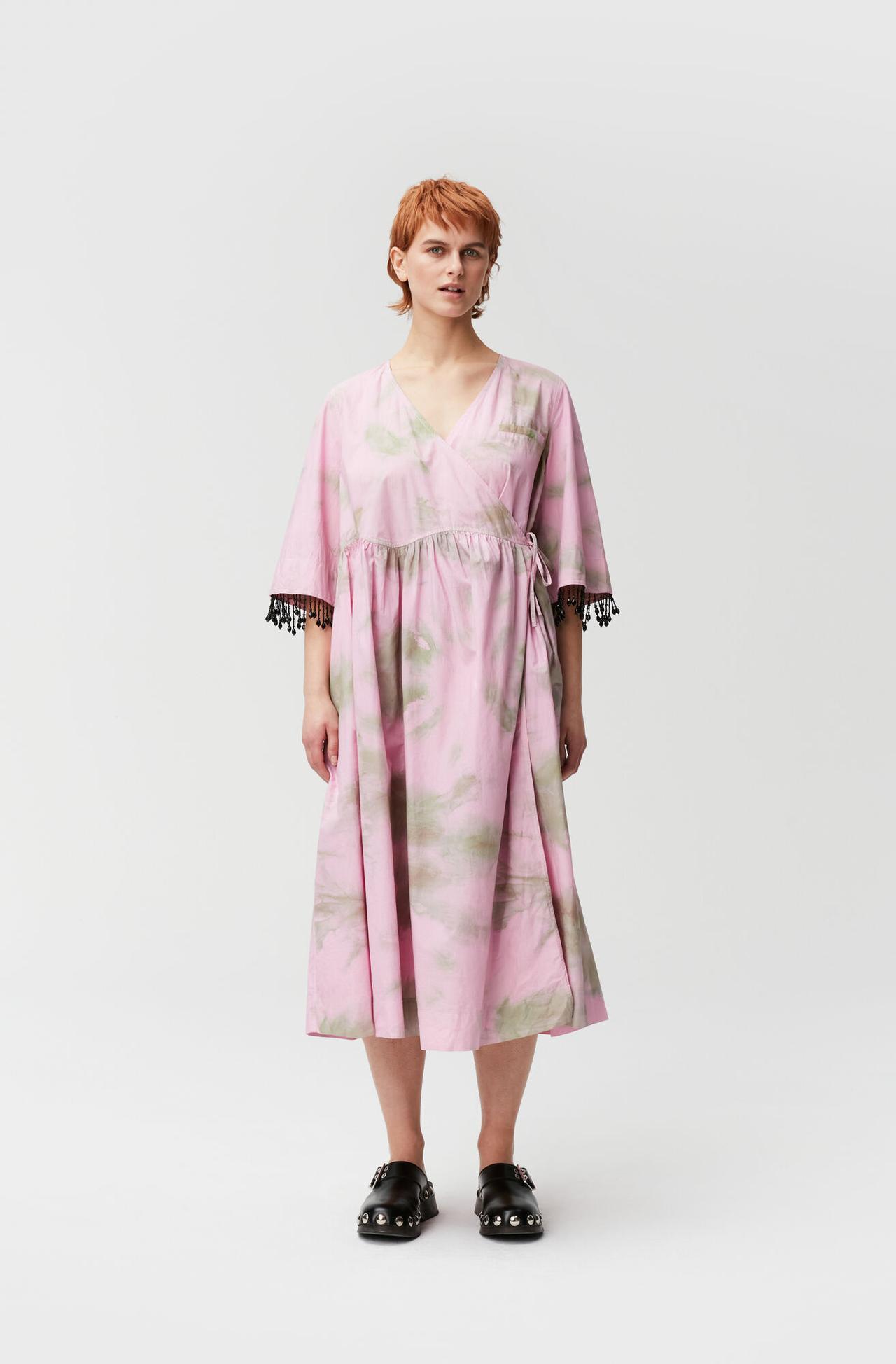 Image of a model wearing an oversized wrap poplin dress in pink and green tie dye with sleeves embellished with black beaded fringes 