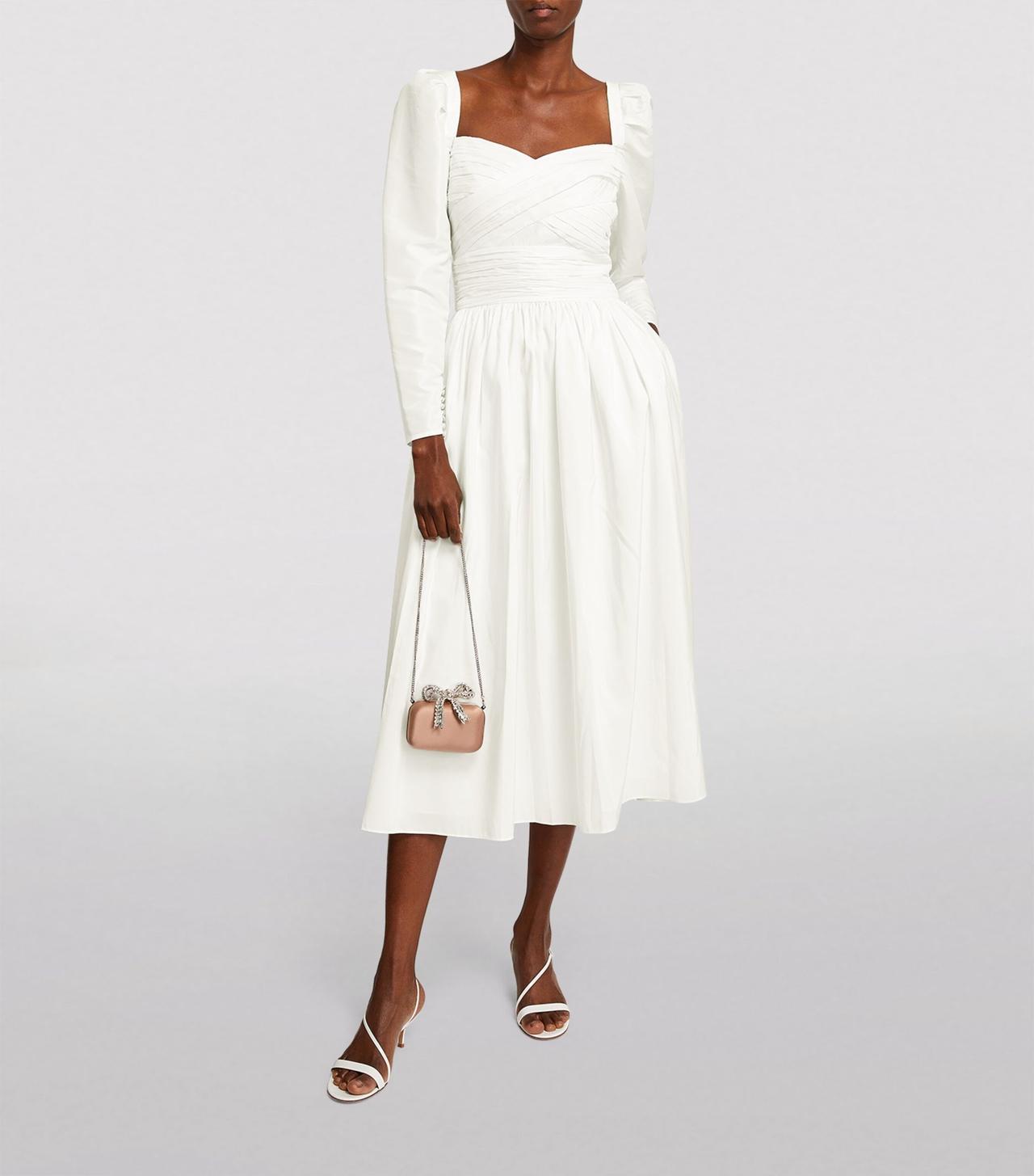 Black woman wearing a long sleeves white taffeta midi dress with a sweetheart neckline and small pink bag with a crystal bow top
