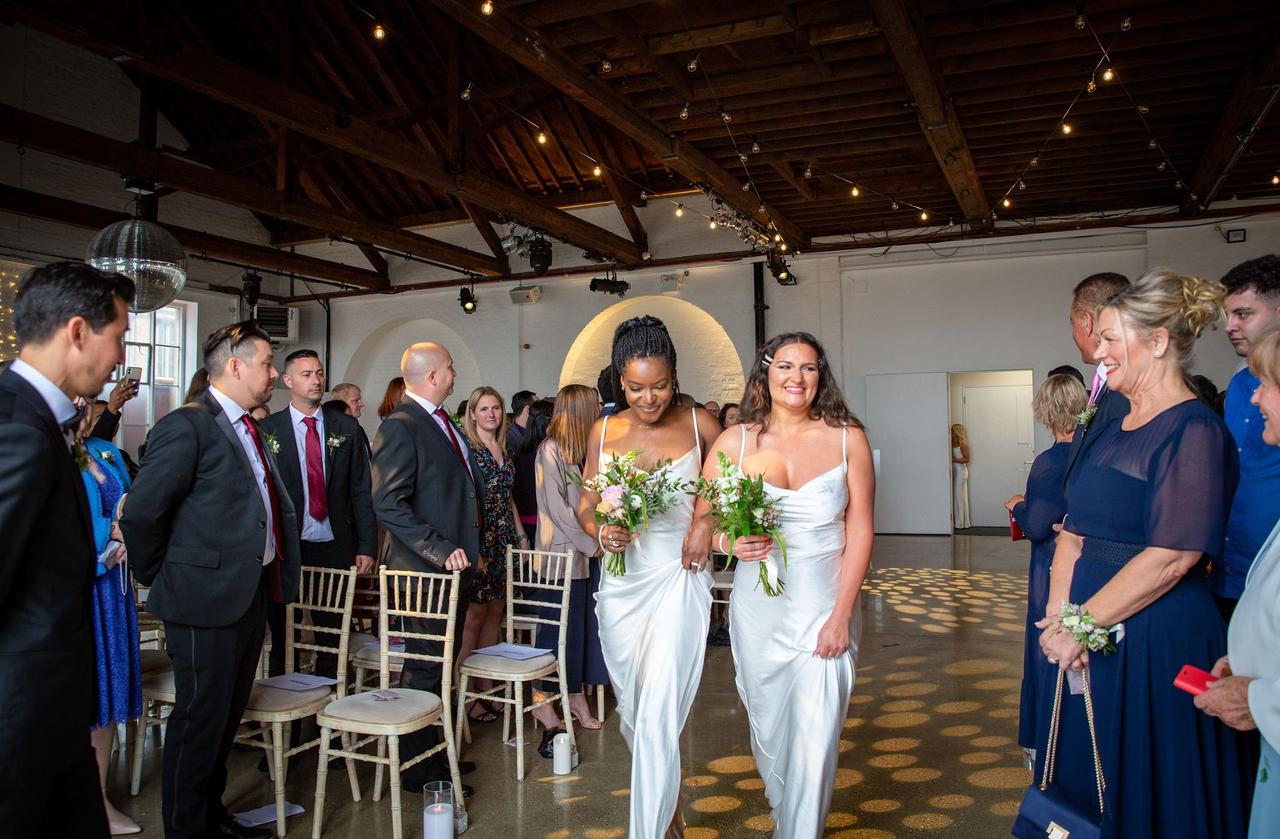 Bridesmaids wearing ivory walk down the aisle with their bouquets