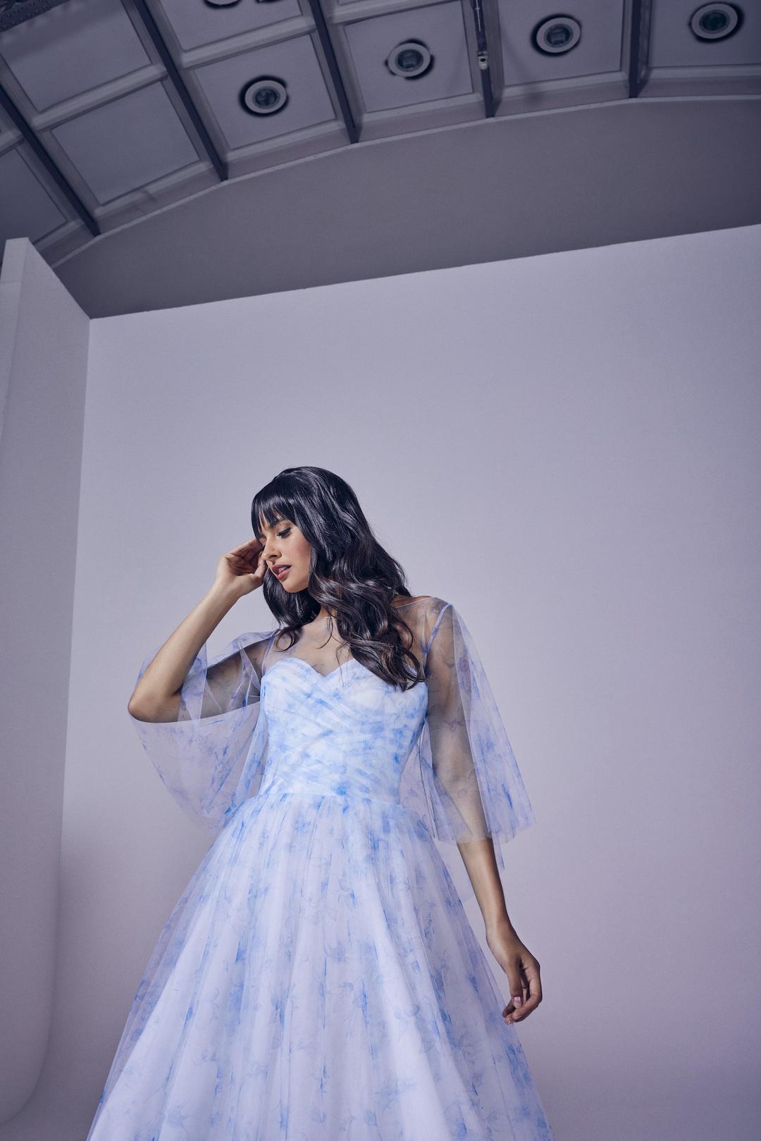 Olive skinned woman with long black hair a fringe wearing a light blue and white tulle strapless wedding dress with a sweetheart neckline and a sheer blue and white tulle jacket