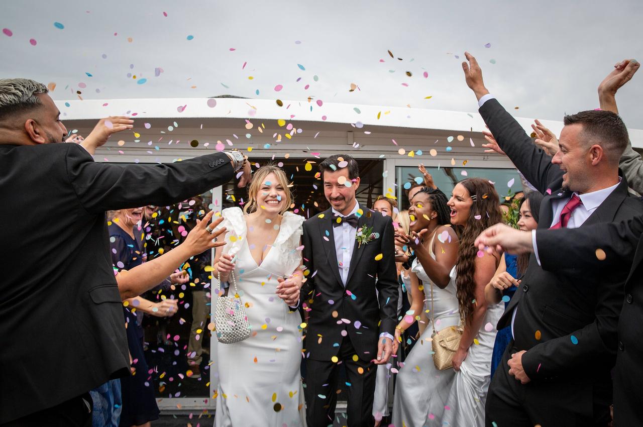 A bride and groom walk through two lines of guests as confetti is thrown