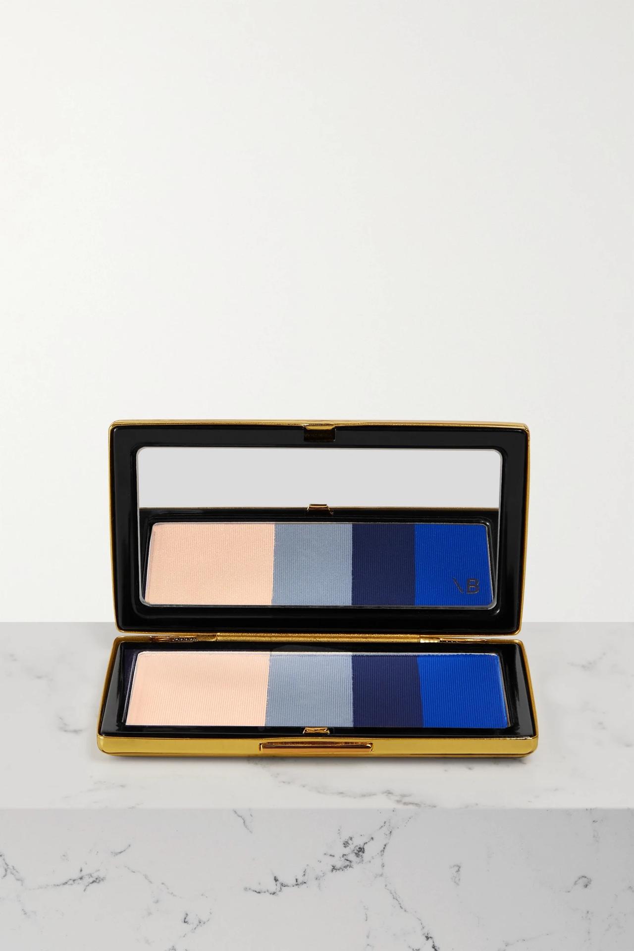 Long gold and mirrored eyeshadow palette with nude, light blue, navy blue and bold electric blue eyeshadows on a marble table
