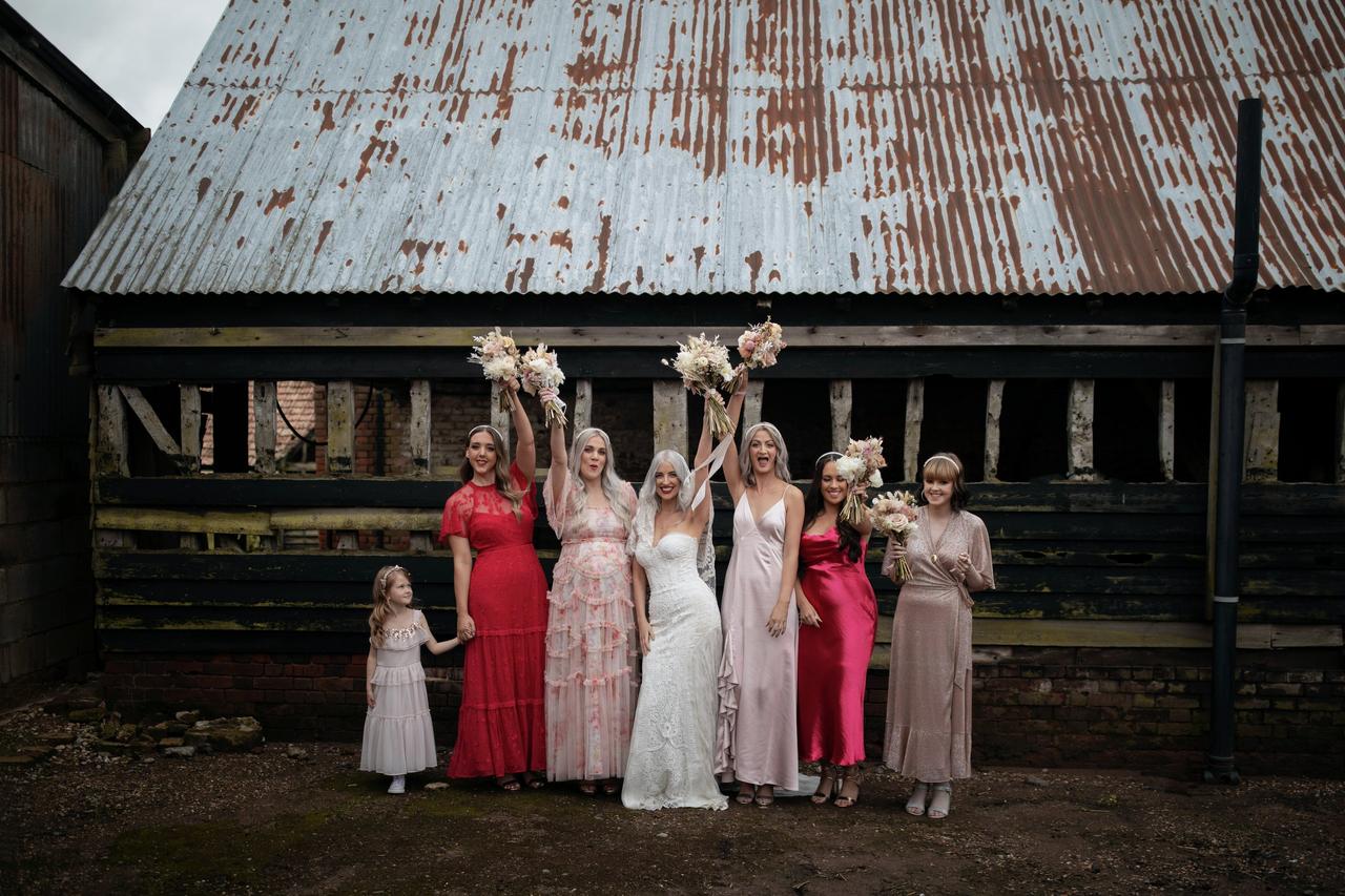 Bride with bridesmaids in pink and red dresses standing outside of a barn