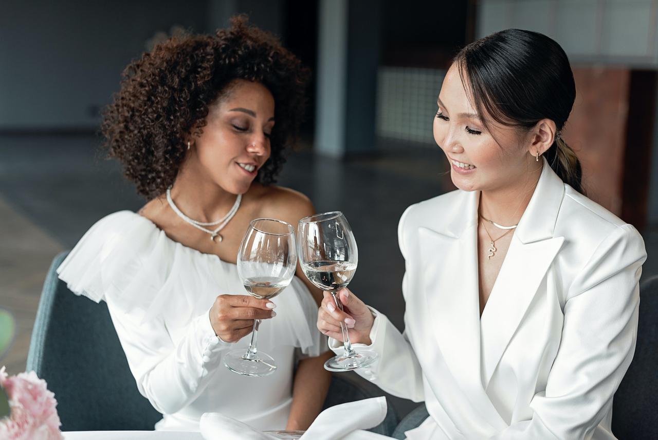 Two brides, one in a suit, cheersing with their wine glasses