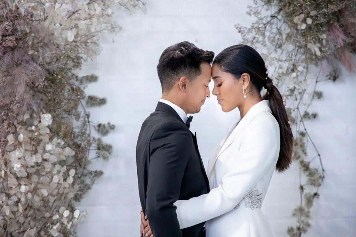 a bride and groom with their heads touching and holding each other in front of winter flowers and a white wall
