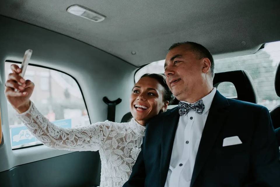 A bride and her dad taking a selfie on the way to her wedding in the car