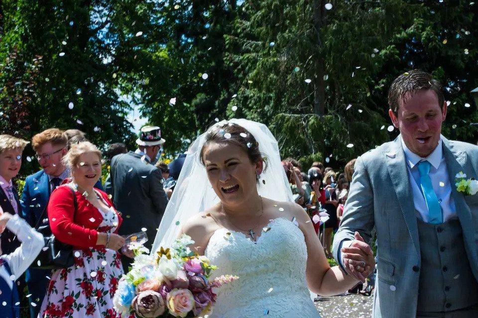 Bride and groom walking hand in hand through a crowd of their guests throwing confetti