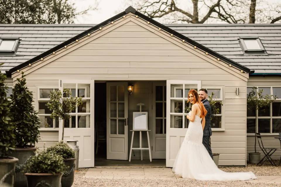 a bride and groom linking arms in front of a white barn hosting their small wedding party 