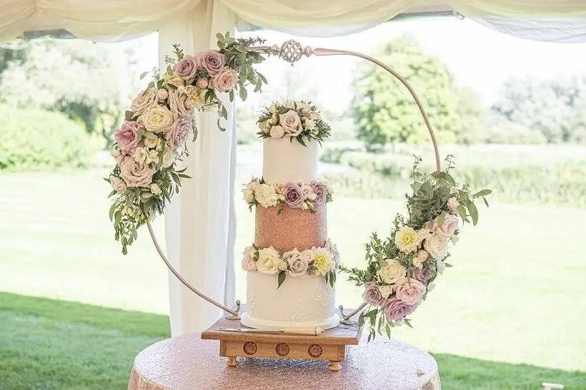 Three tier white and rose gold tier with middle rose gold glitter tier. Decorated with white, pale pink and lilac flowers and a cake hoop