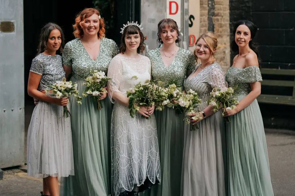 a bride in a beaded wedding dress with five bridesmaids in sage green and grey bridesmaid dresses
