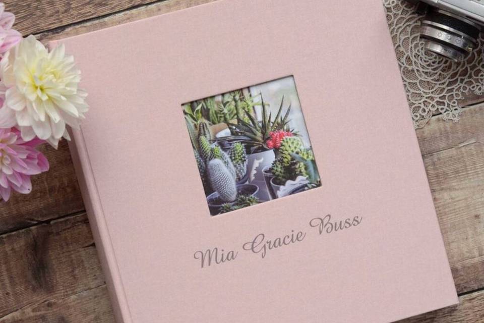 A pink linen photo album with a square window for a photo and a name engraved on the front