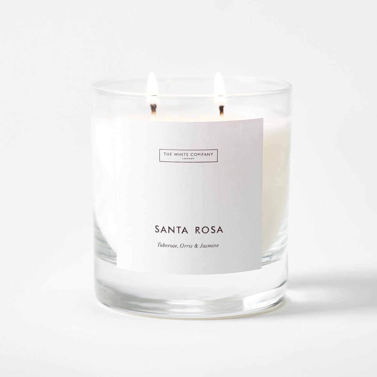 A white candle in a clear glass holder that reads Santa Rose in a neat black font.
