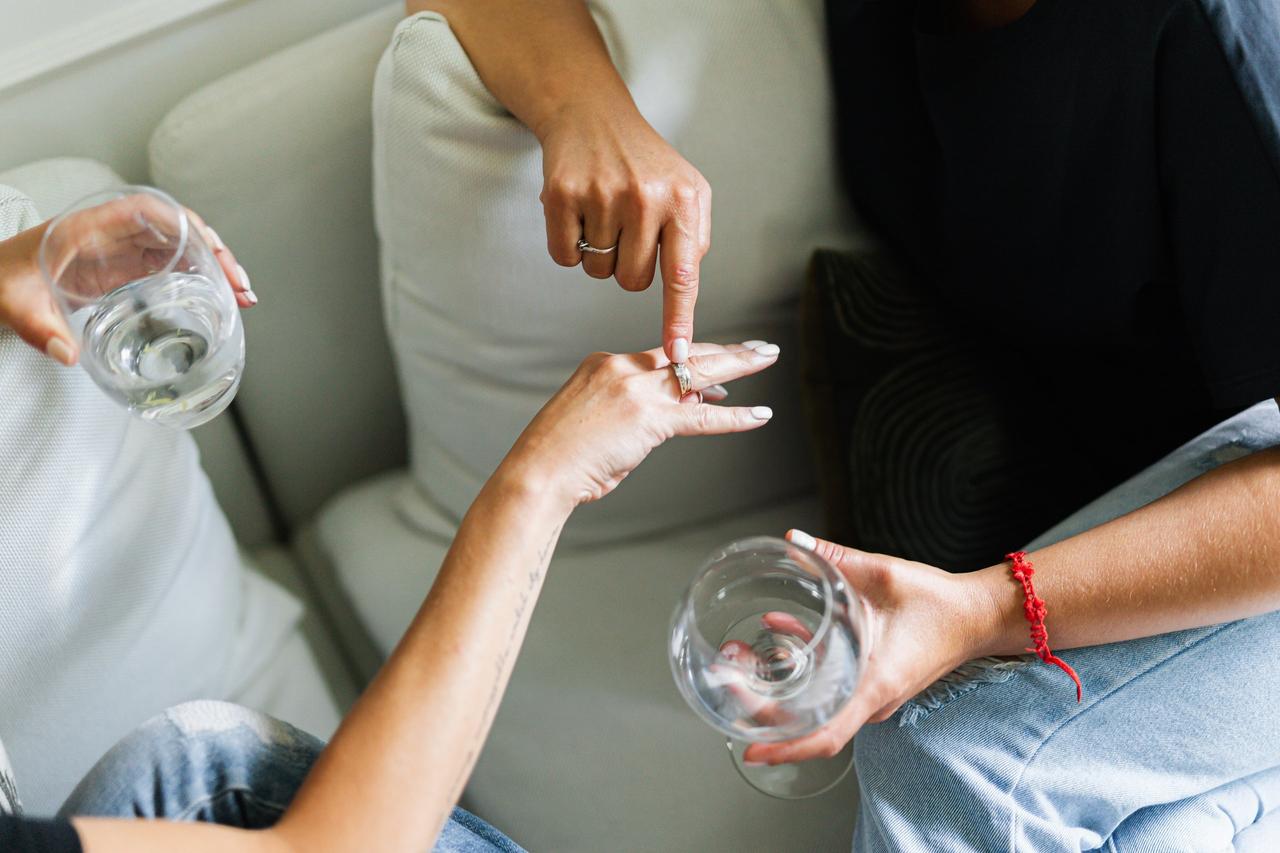 Couple st on a sofa with glasses of wine discussing engagement ring