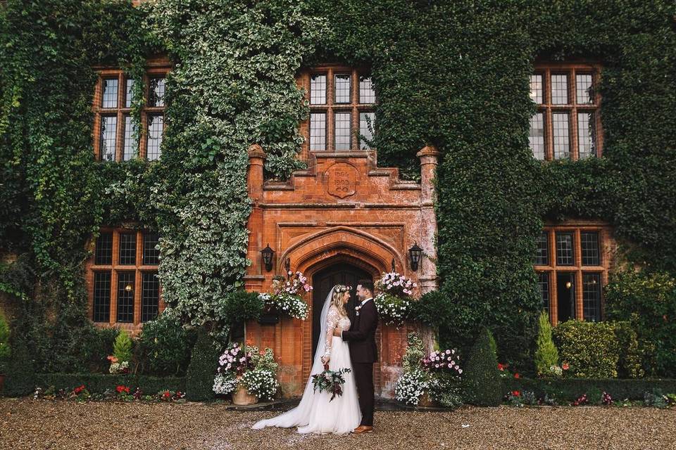 Newlywed couple outside the wedding venue, which features a grand door and five windows that peek out of the greenery that has encased the building