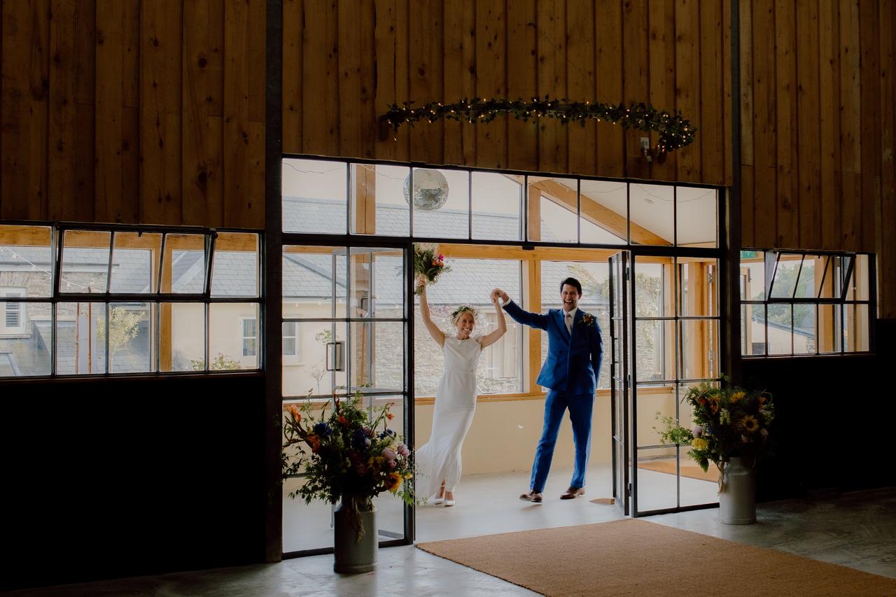 A newlywed bride and groom waving their hands in the air as they enter their wedding reception.