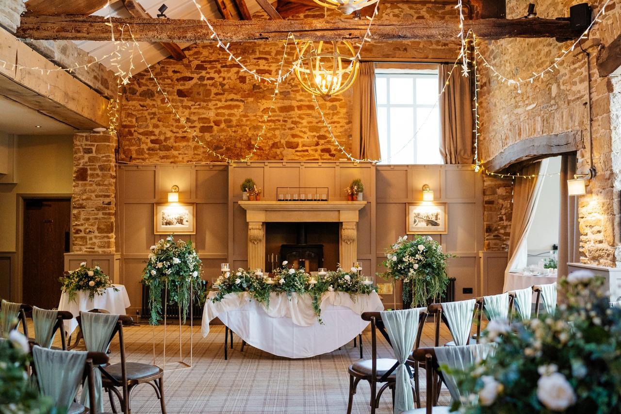Interior of a ceremony room at a pub wedding venue with exposed brickwork, fairylights and elegant draped chairs.