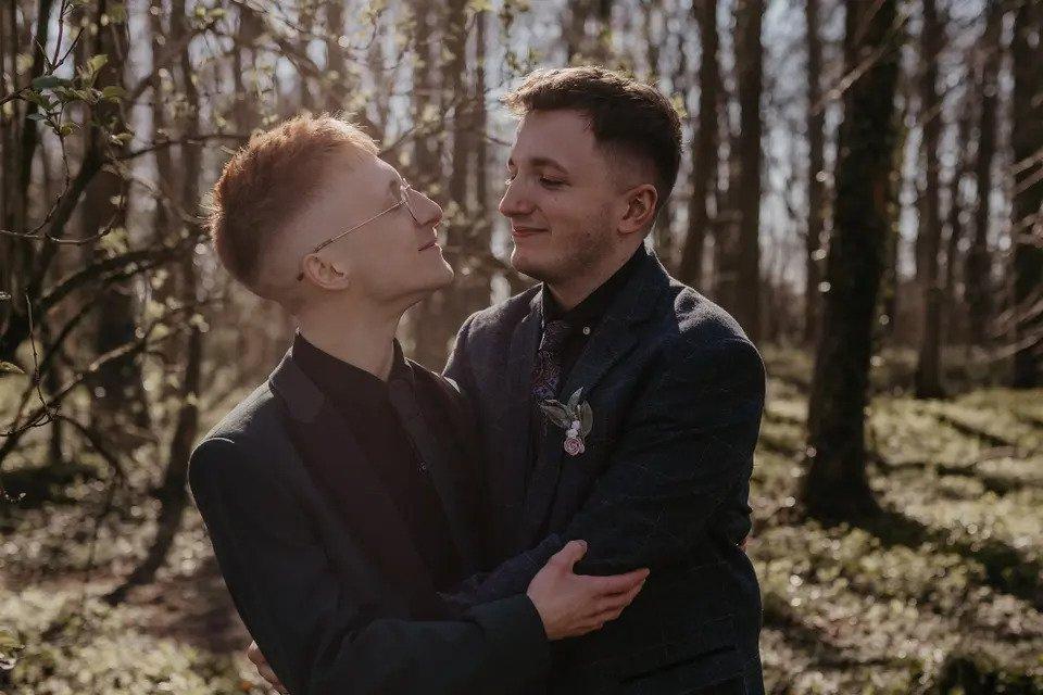 two grooms embrace each other in a forest