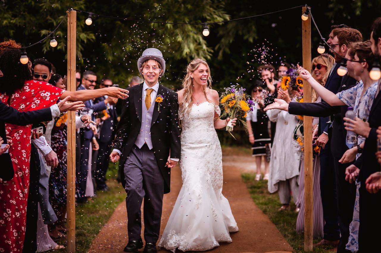 The bride and groom walk through their guests as they throw confetti