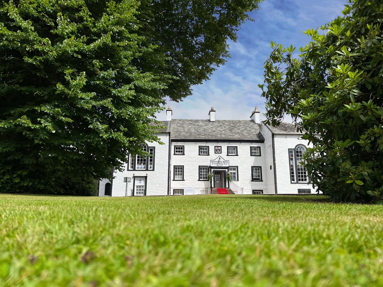 A white country house hotel exterior surrounded by greenery in Gretna Green.