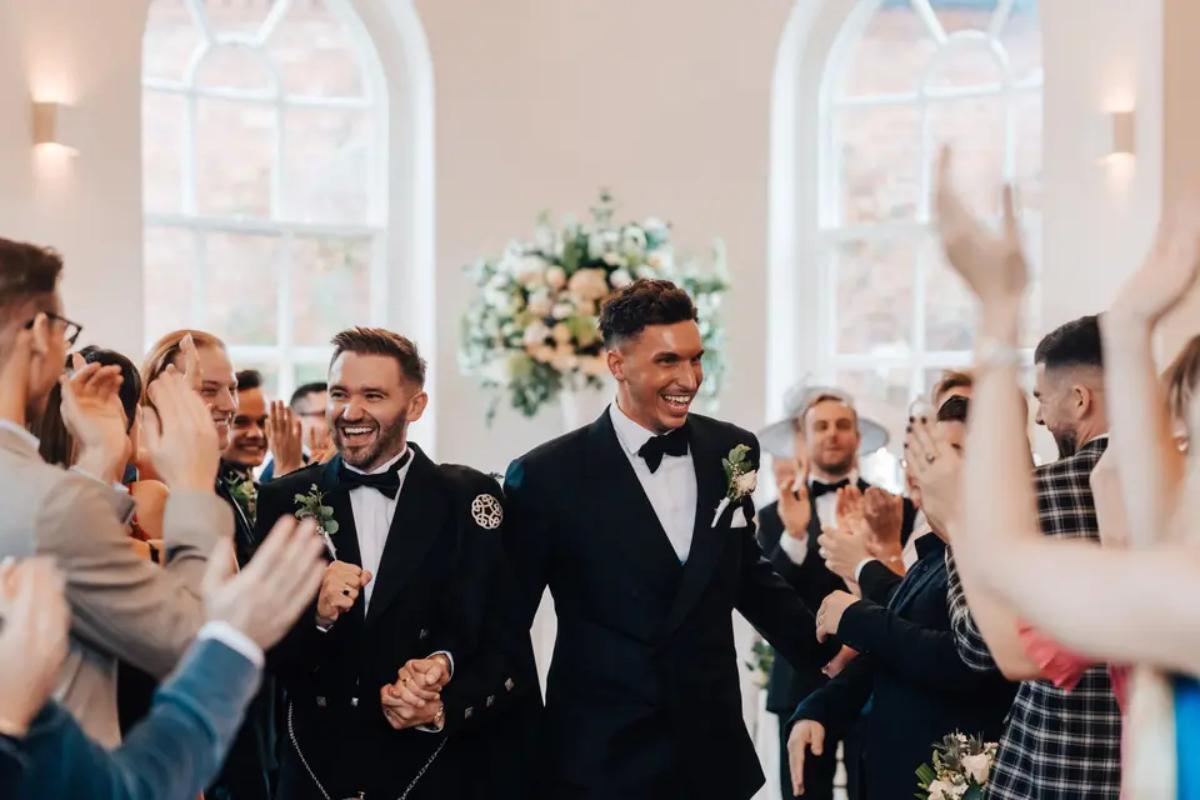Two grooms walking out of their wedding ceremony smiling walking hand in hand