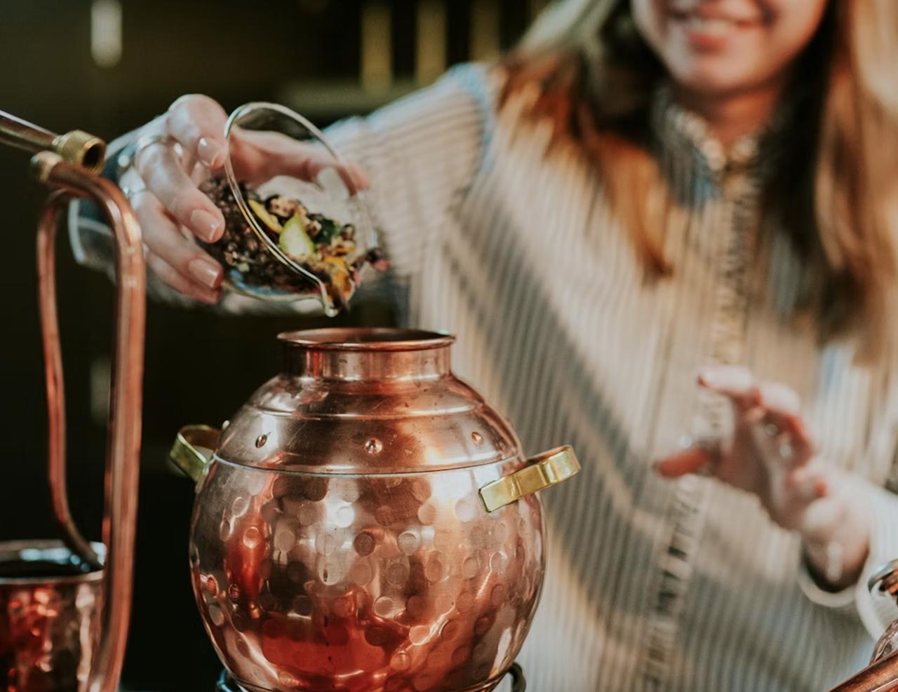 woman smiling as she tips ingredients into a pot during a gin making experience