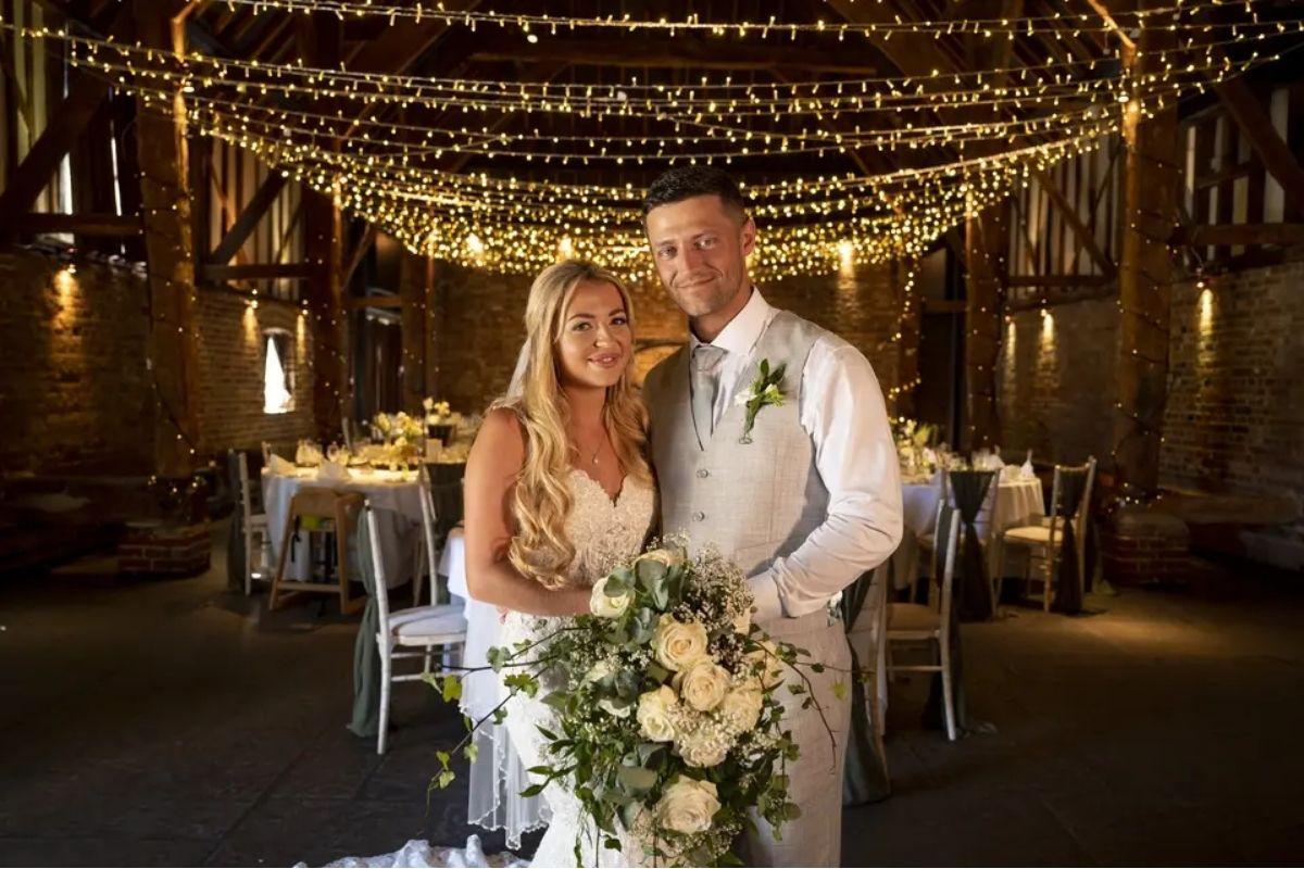 a bride and groom posing next to each other with their fairy-lit wedding breakfast room in the background
