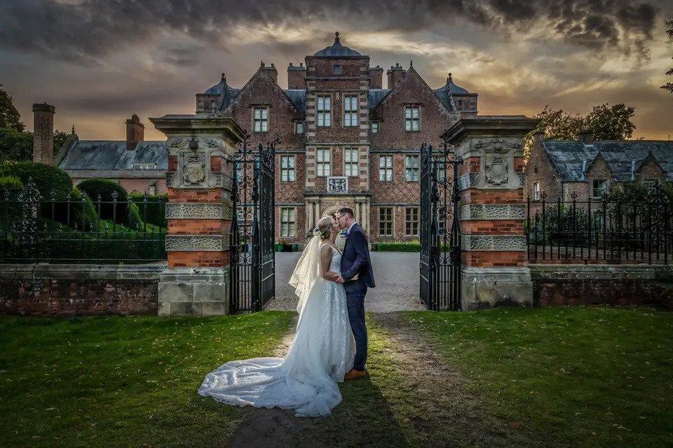 Dramatic wedding photo of a bride and groom kissing outside the gates of a large wedding venue in the North East