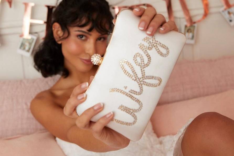 Model holding a white clutch bag with 'wifey' in rhinestones