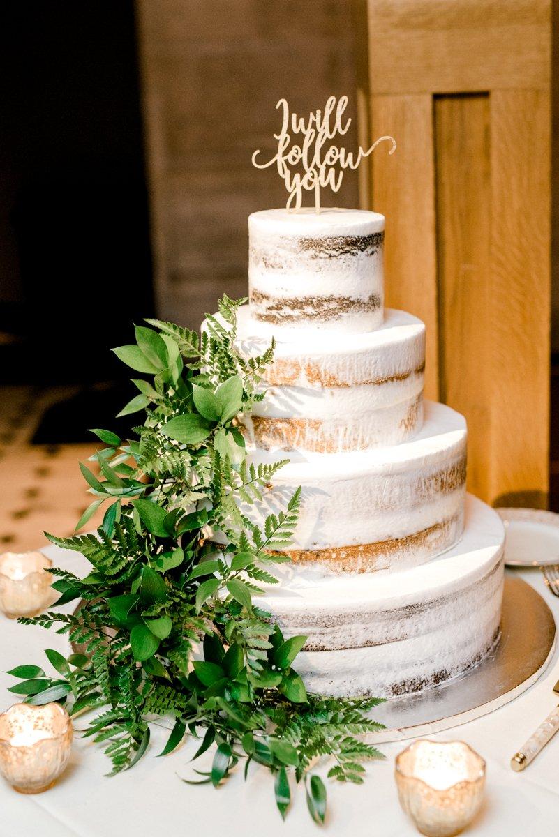 Four tiered semi naked rustic wedding cake with green foliage