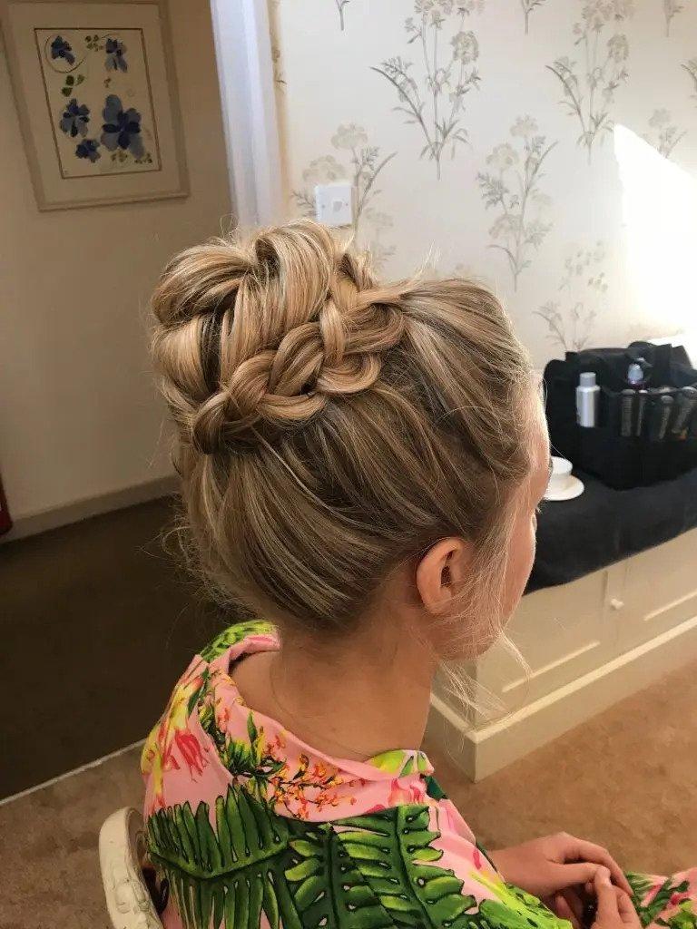 Back of a bride's head with blonde hair in a high bun with a thick plait around the base