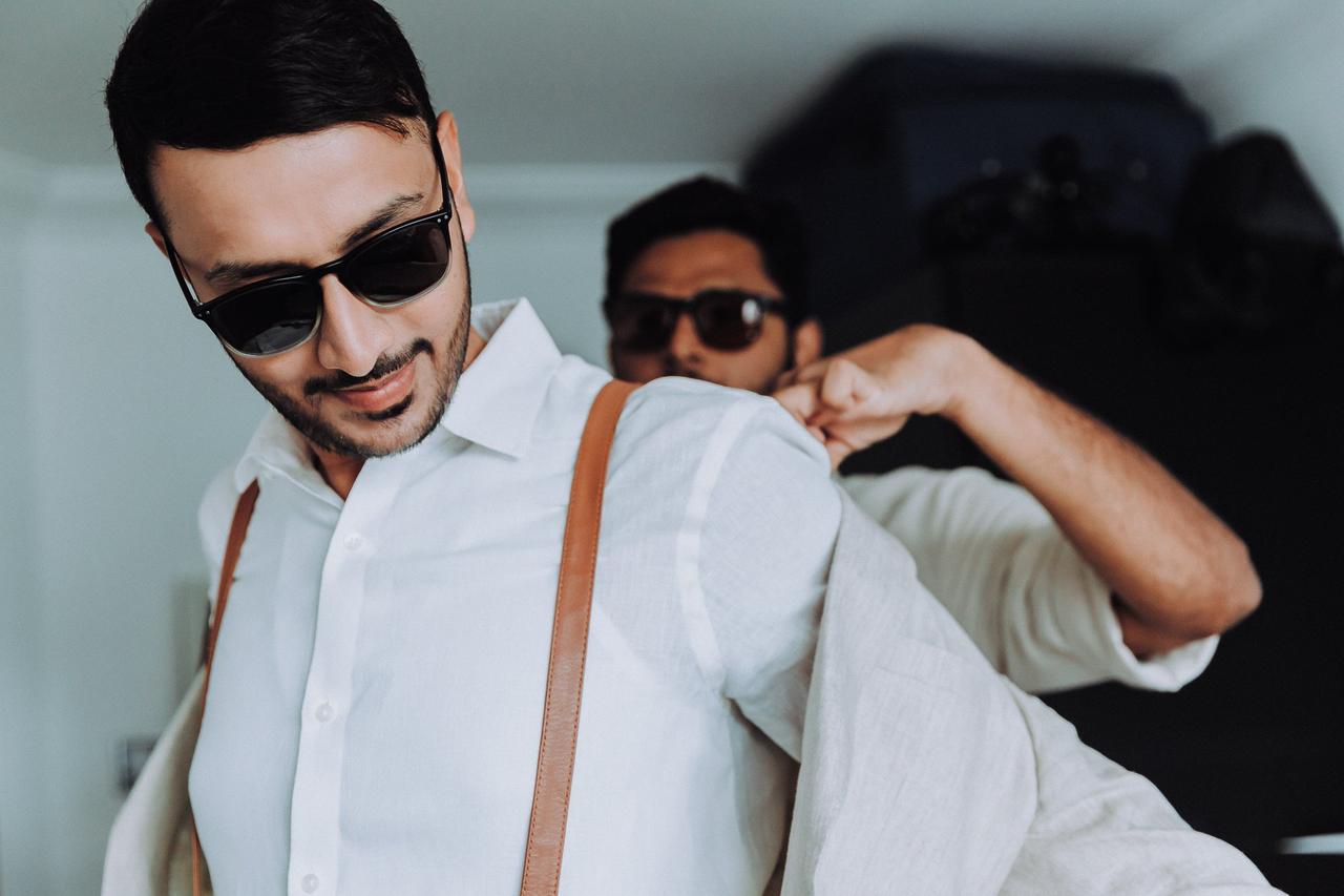 A groom having help with his jacket from his best man.