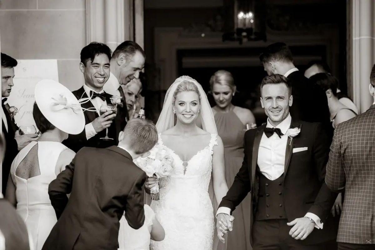 a black and white photograph of a bride and groom exiting their wedding ceremony with guests around