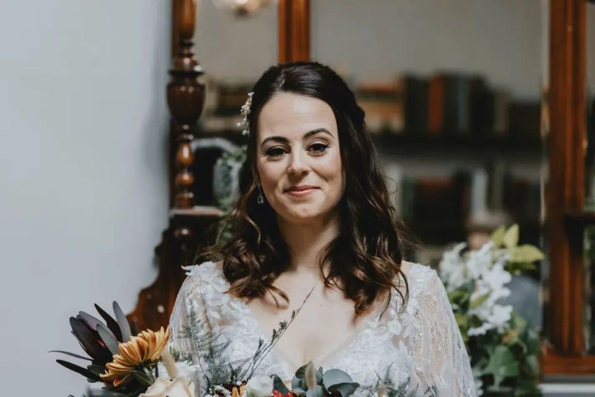 a beautiful brunette bride posing in the center of the shot with natural radiant amkeup and flowers and a mirror in the background