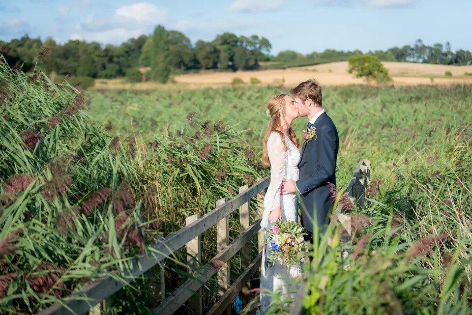 Bride and groom kiss on a bridge in the middle of tall plants