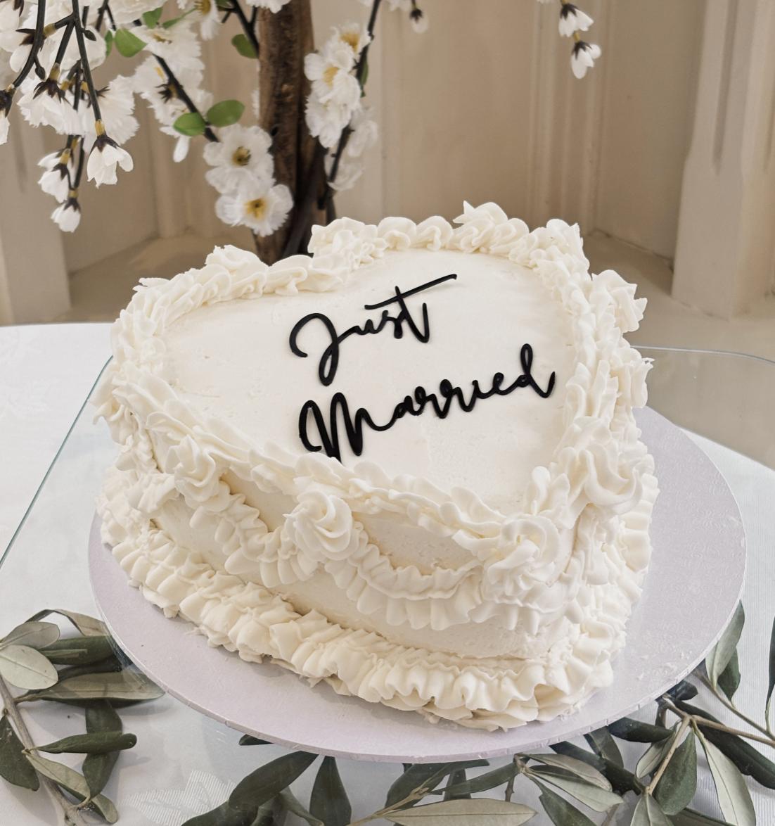 A white heart shaped wedding cake with 'just married' in black icing.
