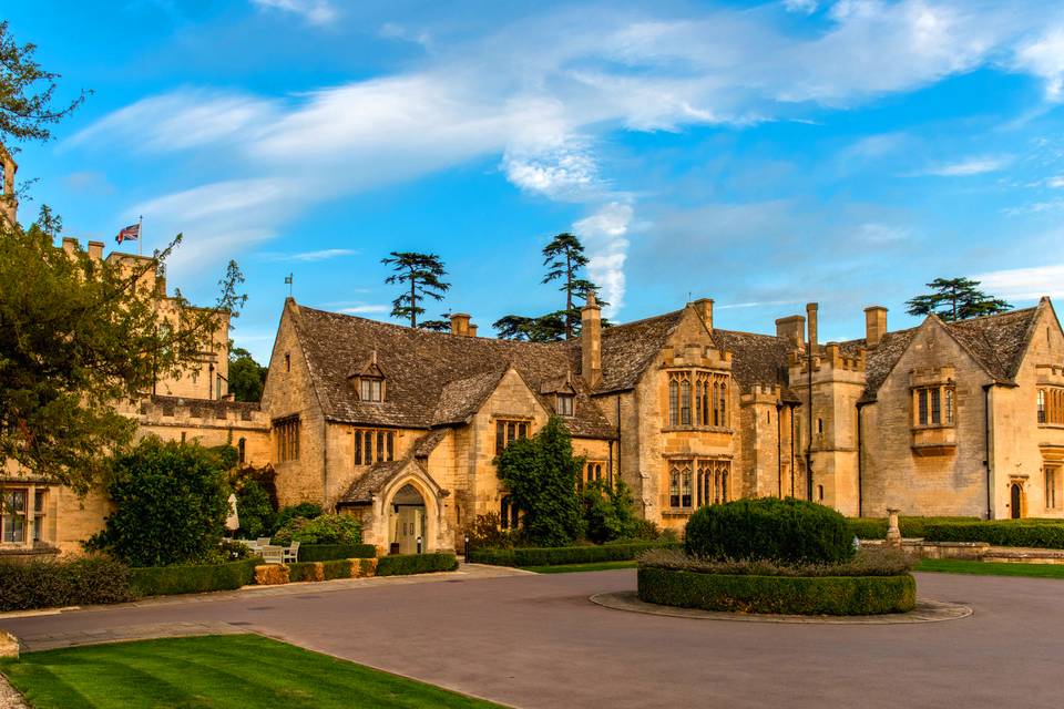 Exterior view of five star cheltenham hotel and wedding venue Ellenborough park. the period sandstone building is surrounded by greenery against a bright blue sky