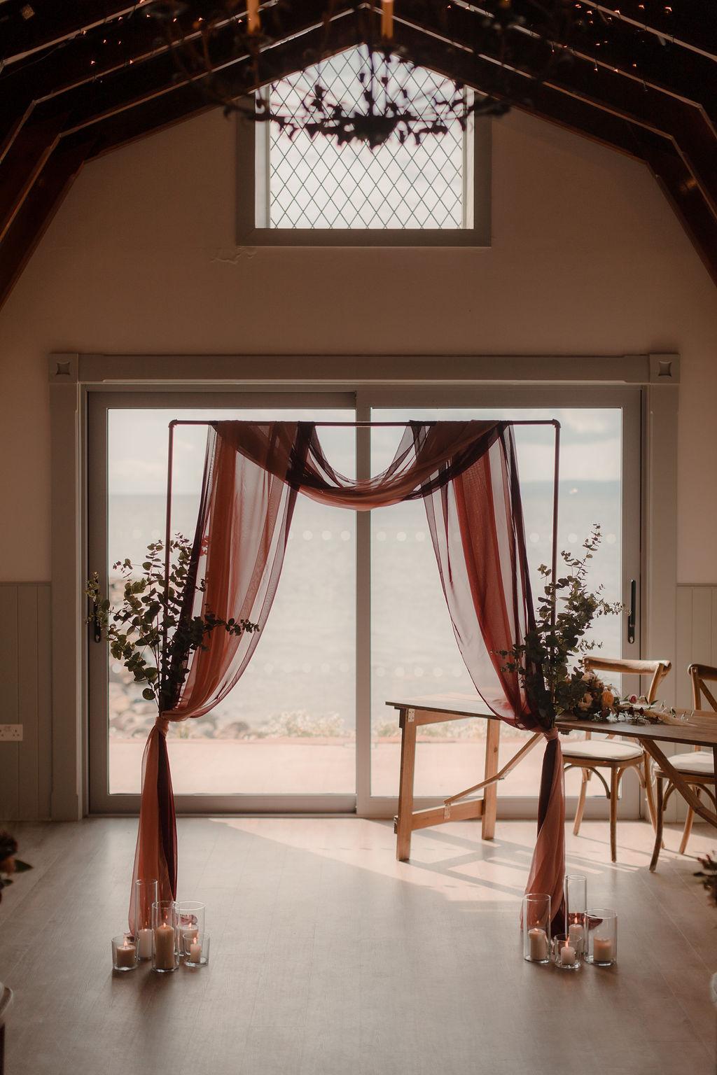 Metal rectangular frame with simple burgundy voile and eucalyptus decor 