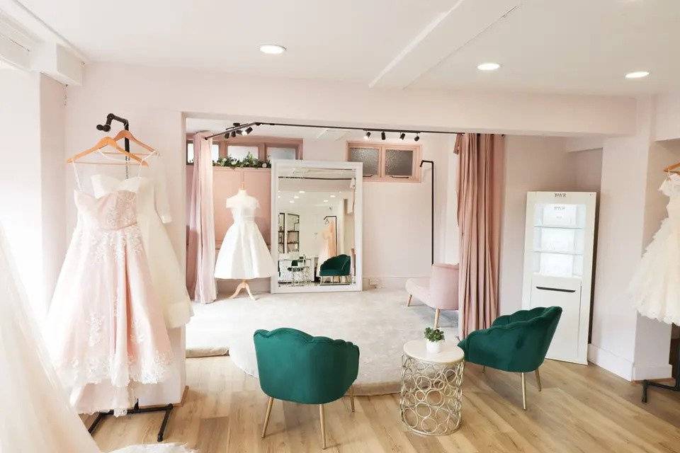 An interior shot of a bridal boutique with wedding dresses on mannequins and dark green velvet chairs to sit in 