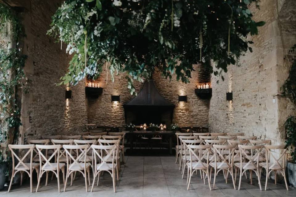 the ceremony room at stone barn which has white brick walls, light wooden chairs and a large foliage instalment 
