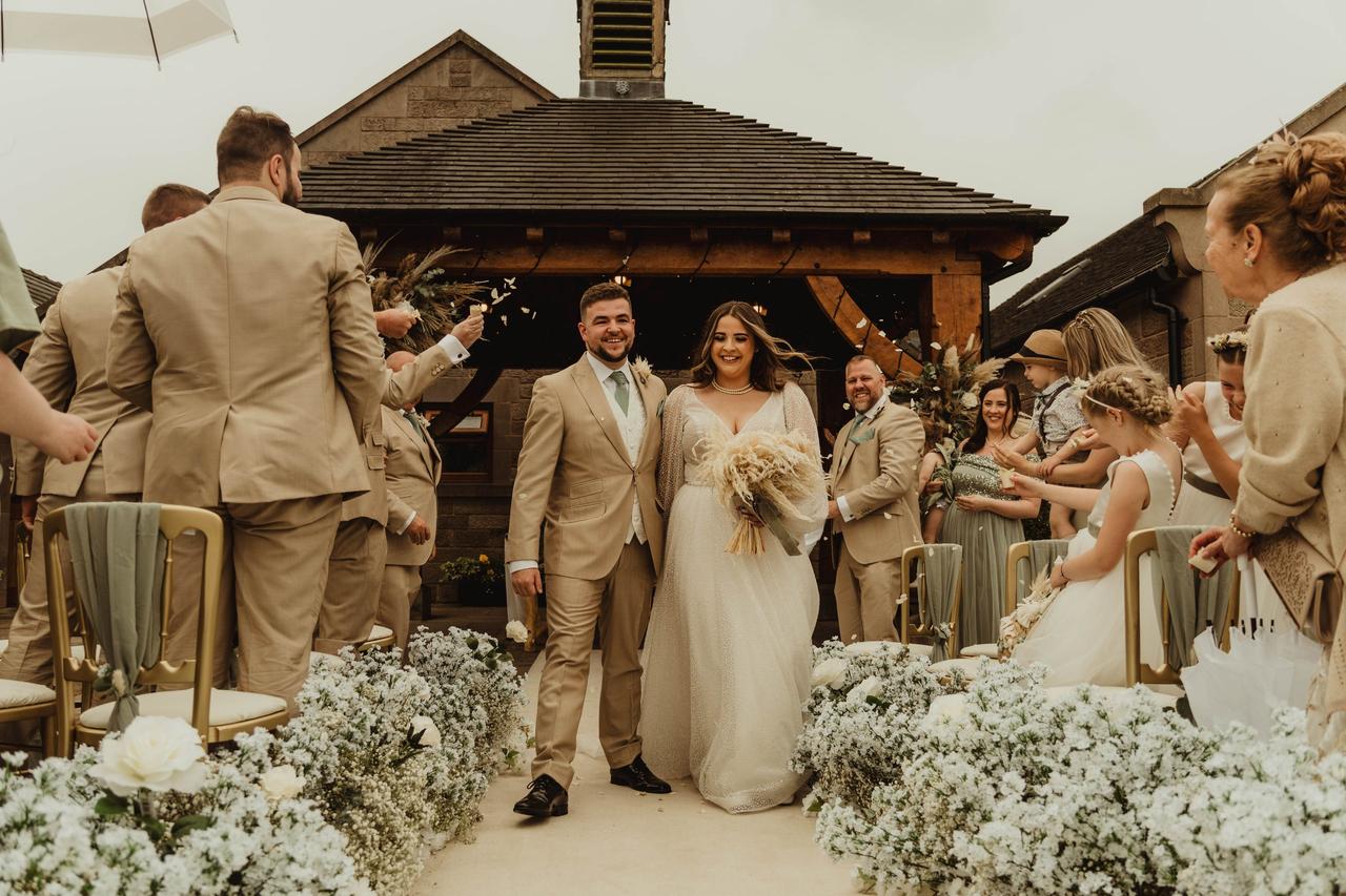 A bride and groom exiting their outdoor wedding ceremony as guests throw confetti on them