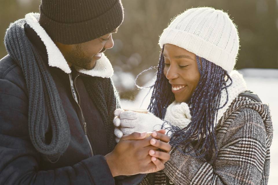 a couple enjoying a winter date holding coffees and outside in the snow 